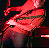 Fretting up high Ricky strikes the PRS electric guitar with assertion, intent and unforgiveness in a red wash light - CanningMusic photo archive